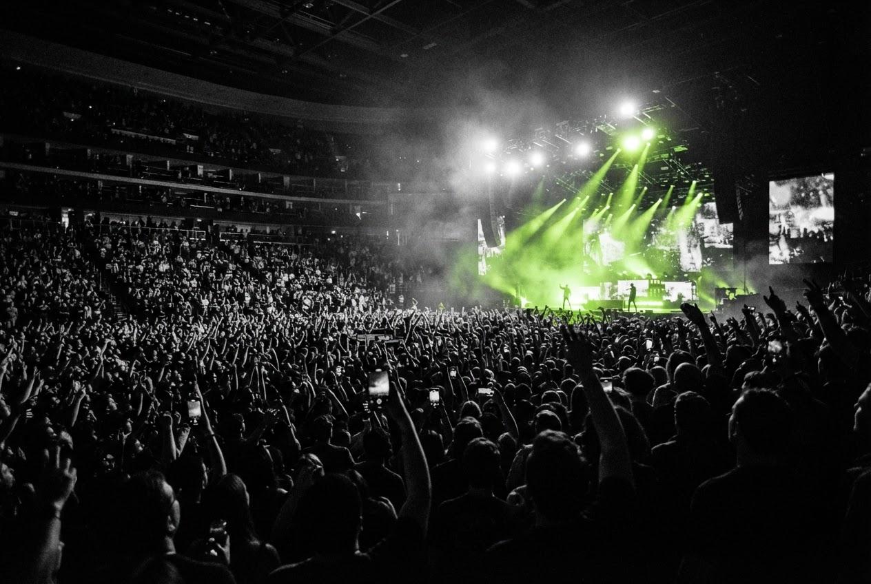 A packed arena under green stage lights